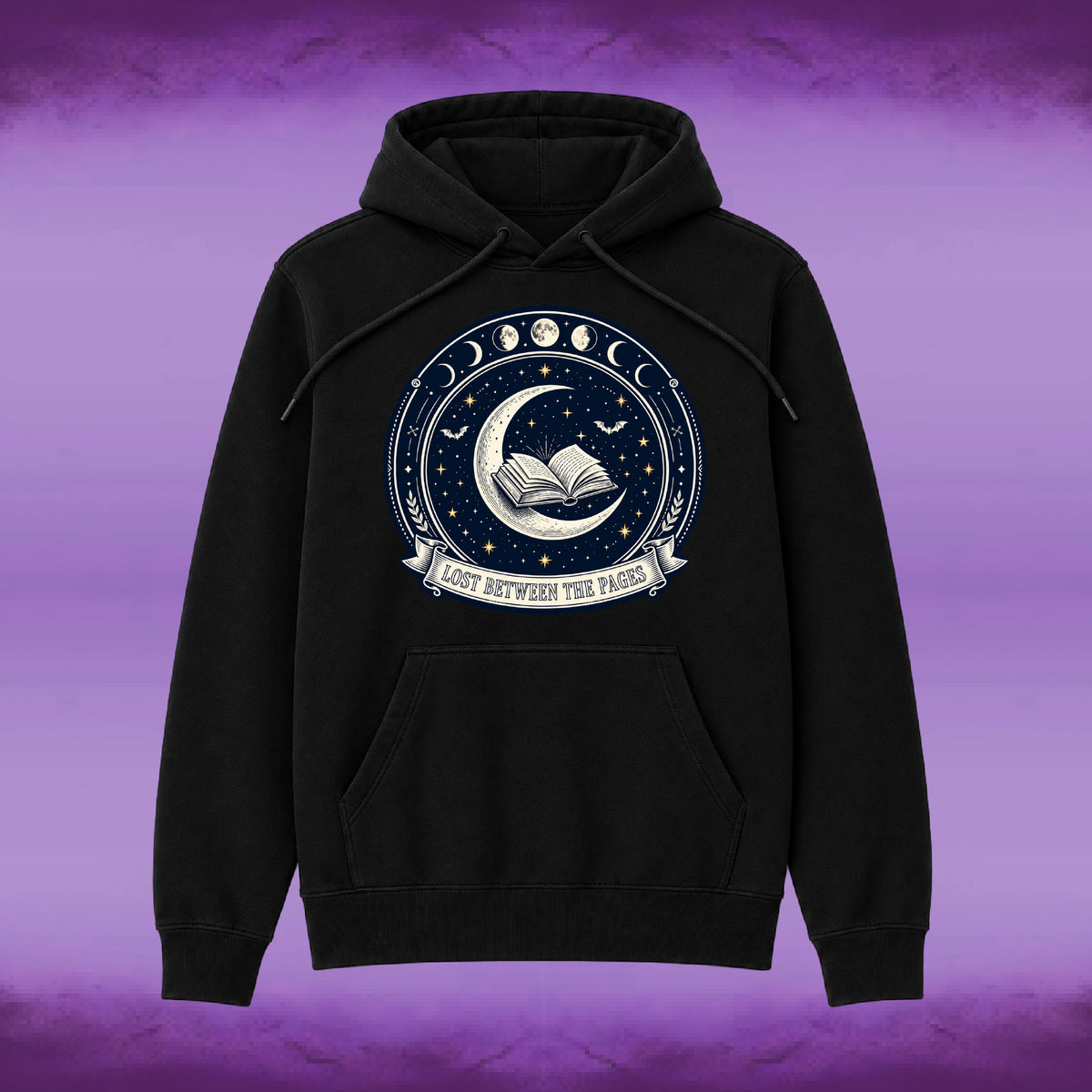 A black pullover hoodie with a circular celestial graphic on the chest featuring moon phases, stars, an open book, and the text 'LOST BETWEEN THE PAGES'. The hoodie is displayed against a purple textured background.