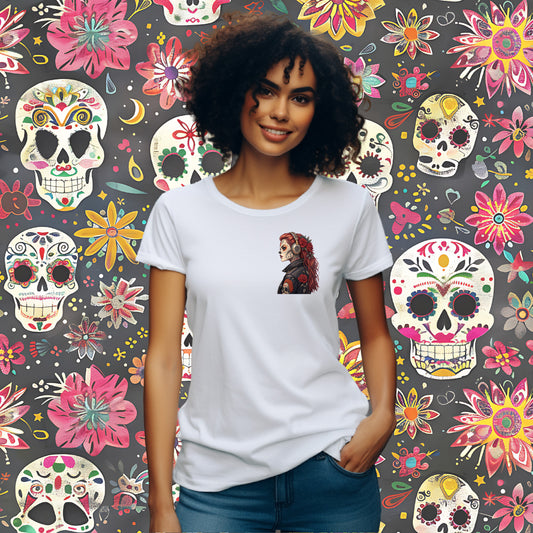 A woman with curly dark hair wearing a white short-sleeve t-shirt with a colorful graphic of a Day of the Dead (Dia de los Muertos) woman on the chest, standing in front of a dark gray background covered in a vibrant, colorful floral and skull pattern.