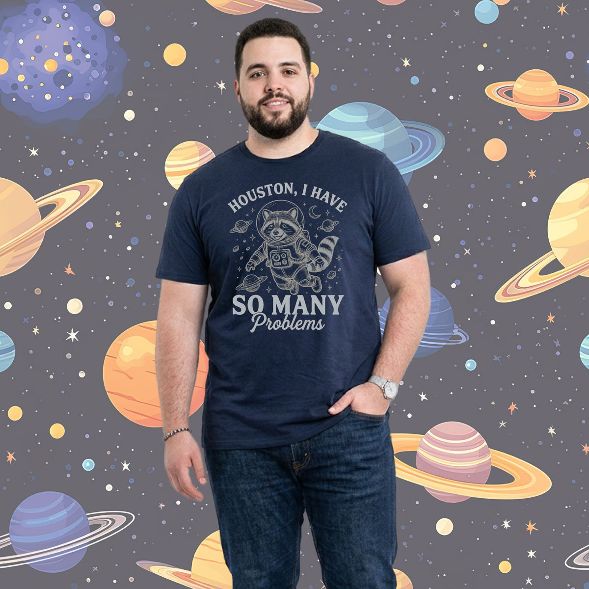 A man wearing a navy blue graphic t-shirt with a cartoon raccoon and the text 'HOUSTON, I HAVE SO MANY Problems' stands against a cartoon space background filled with planets and stars.