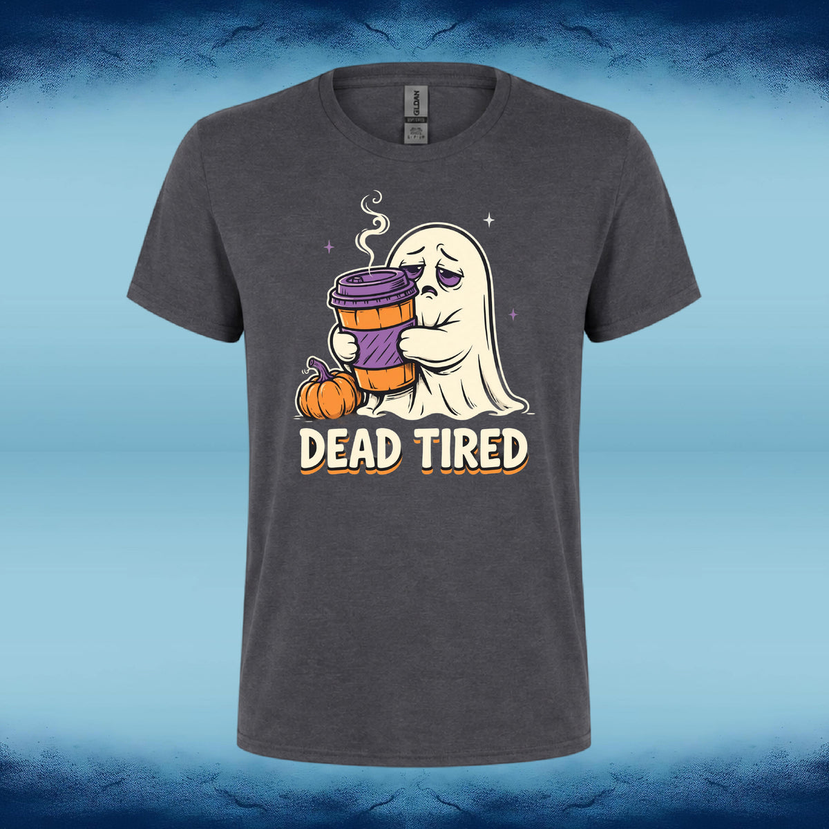 A dark gray crewneck t-shirt featuring a cartoon graphic of a tired ghost holding a purple coffee cup next to a small pumpkin, with the text 'DEAD TIRED' underneath, set against a blue textured background.