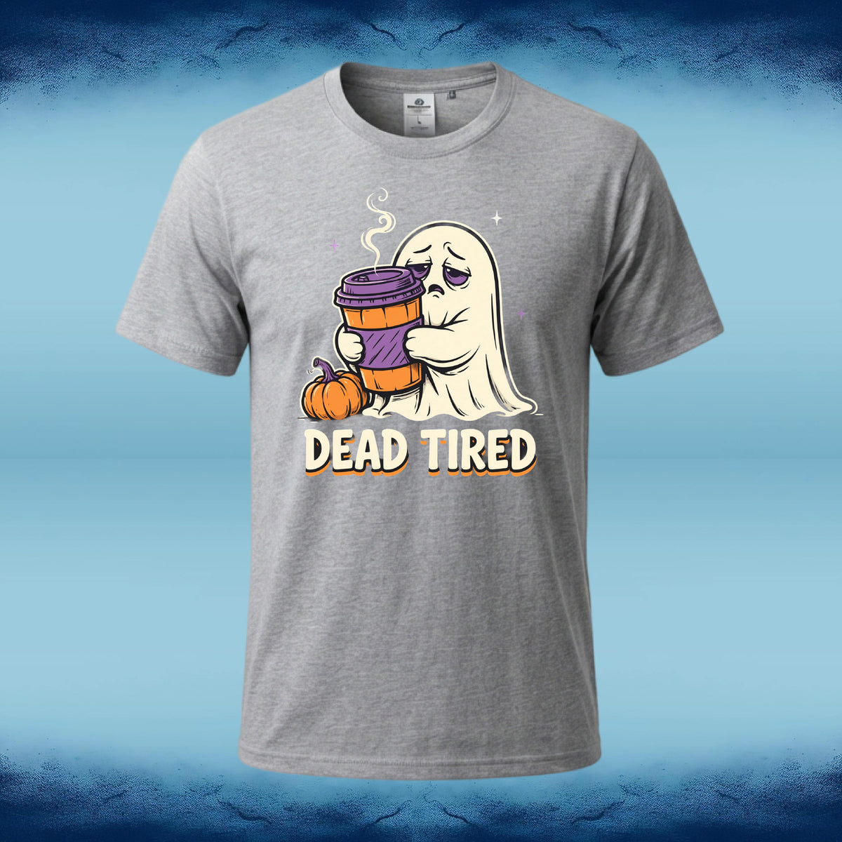 A heather gray short-sleeve t-shirt with a cartoon graphic of a ghost holding a purple coffee cup next to a small pumpkin, with the text 'DEAD TIRED' below. The shirt is displayed against a blue gradient background with dark blue textured borders at the top and bottom.