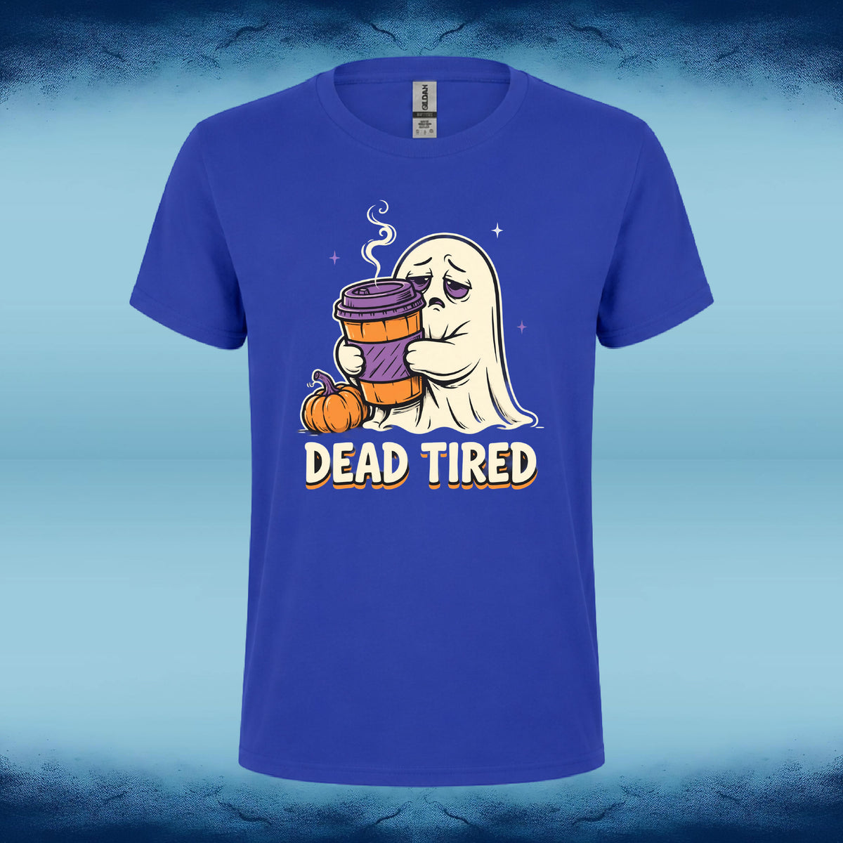 A royal blue short-sleeve t-shirt with a cartoon graphic of a tired white ghost holding a purple coffee cup next to a small pumpkin, with the text 'DEAD TIRED' printed below. The shirt is displayed against a blue and black textured background.