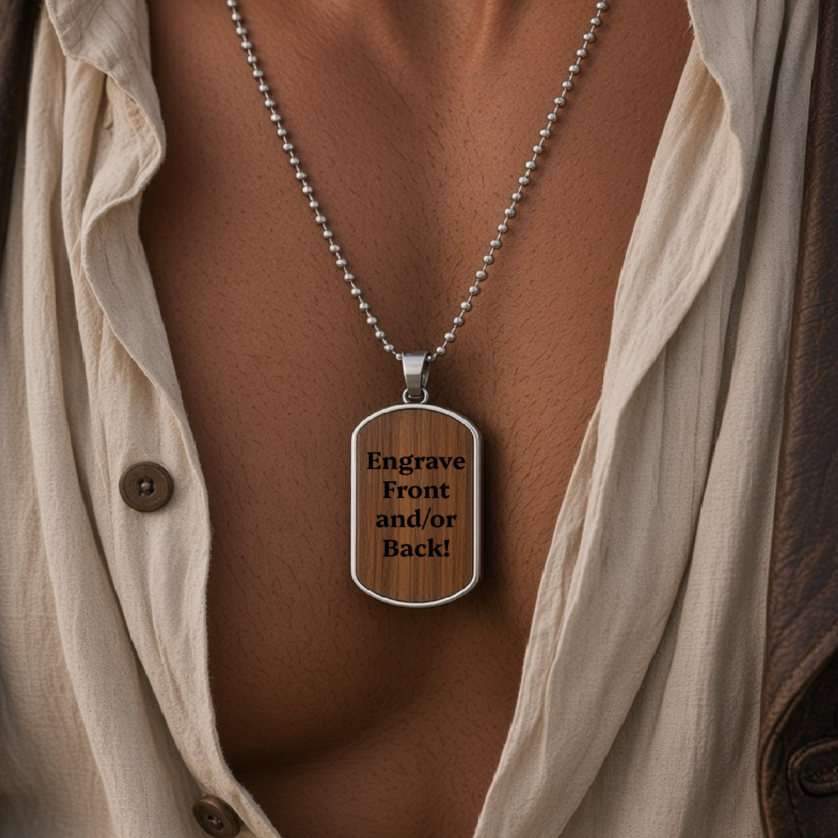 A silver ball-chain necklace with a rectangular dog-tag pendant worn on a person's chest. The pendant has a woodgrain-style insert with black engraved text reading 'Engrave Front and/or Back!'.