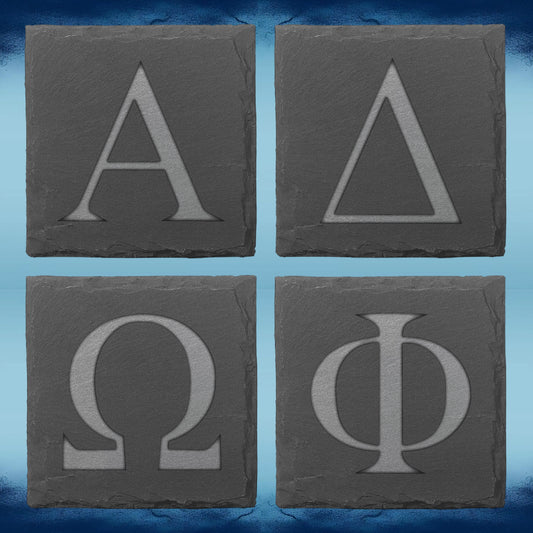 Four square dark gray stone coasters arranged in a 2x2 grid, each engraved with a large Greek letter: Alpha, Delta, Omega, and Phi, on a blue textured background.