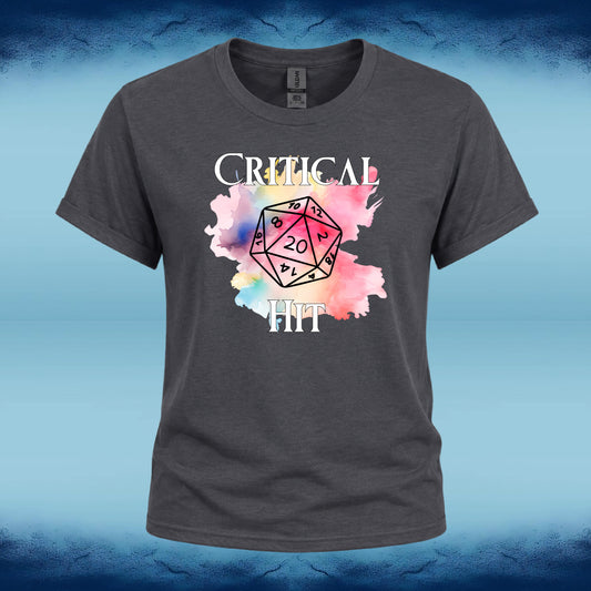 A dark gray crewneck t-shirt featuring a graphic print of a 20-sided die over a pink and blue watercolor splash, with the words 'CRITICAL HIT' in white text. The shirt is displayed against a blue textured background.