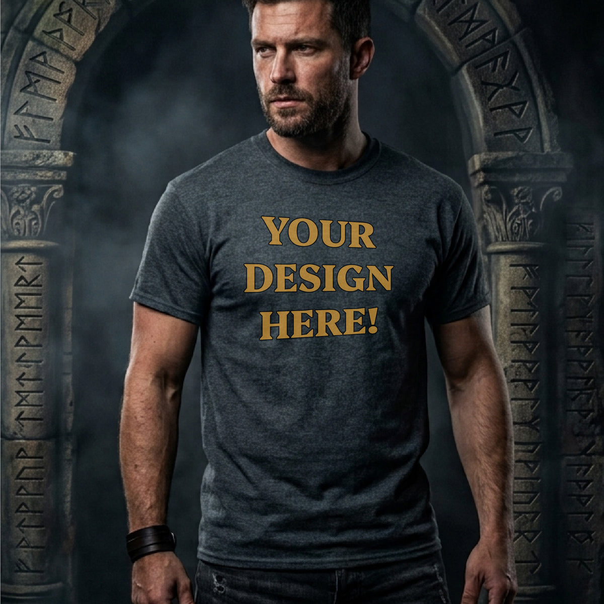A man wearing a dark heather gray t-shirt with the words 'YOUR DESIGN HERE!' printed in gold lettering, posed in front of a dark, gothic stone archway.