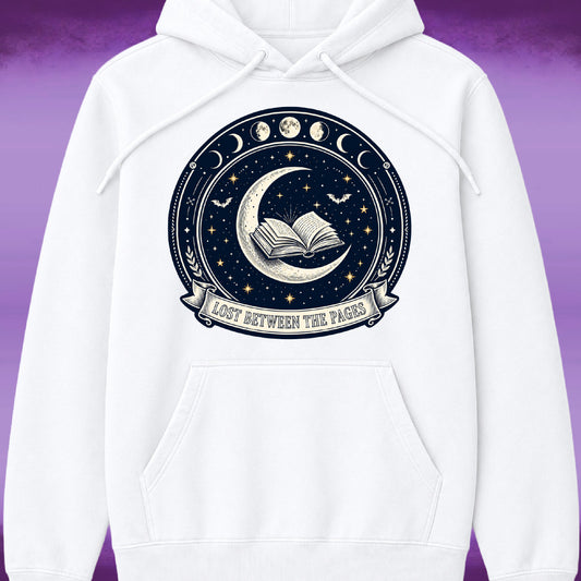 A white pullover hoodie with a large circular celestial graphic on the chest. The graphic features a dark navy blue night sky with a crescent moon, an open book, stars, moon phases, bats, and a banner reading 'LOST BETWEEN THE PAGES'.