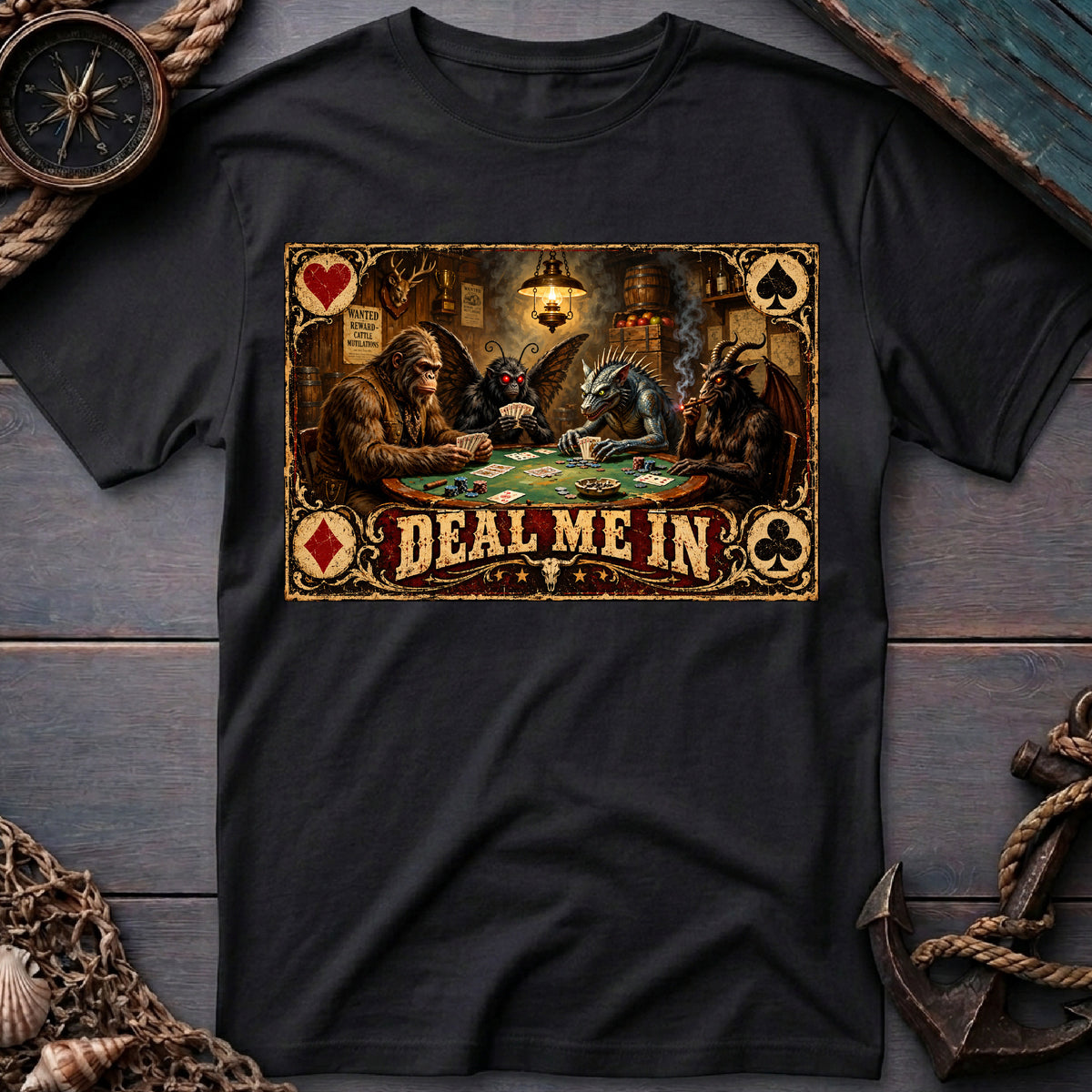 Black graphic tee laid flat with cryptids playing poker and “Deal Me In” lettering, surrounded by nautical props.