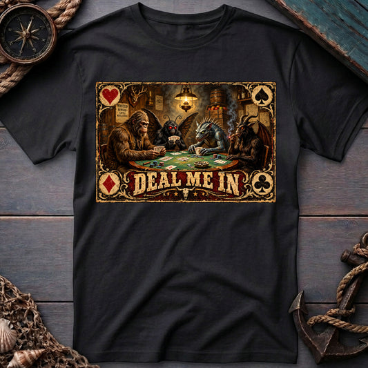 Black graphic tee laid flat with cryptids playing poker and “Deal Me In” lettering, surrounded by nautical props.