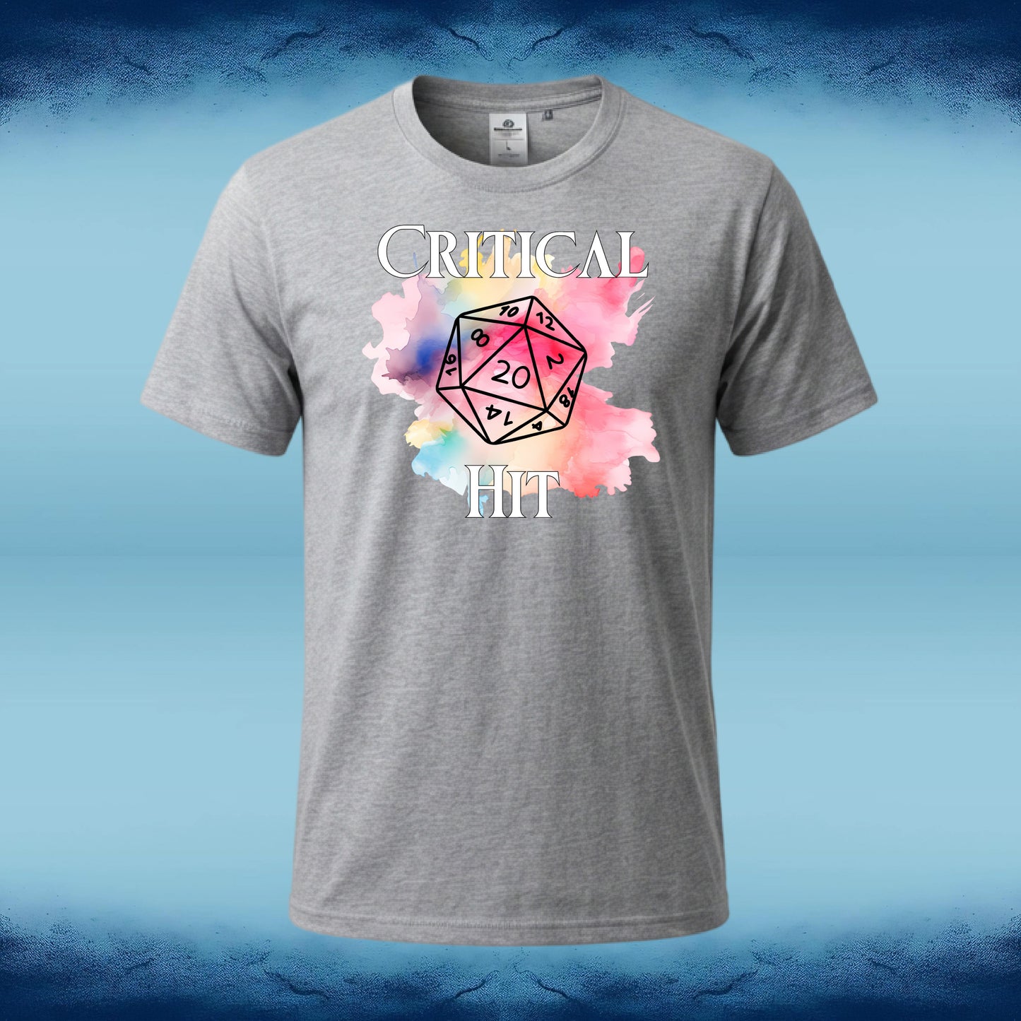 A heather gray short-sleeve t-shirt with a graphic on the front featuring the text 'CRITICAL HIT' and a watercolor-style multicolor die with a 20. The shirt is displayed against a blue gradient background.