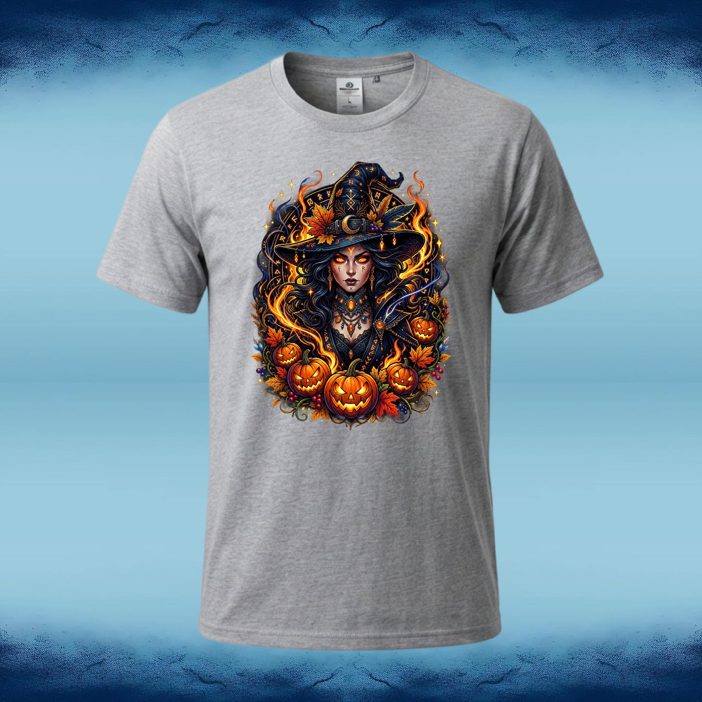 A heather gray short-sleeve t-shirt with a detailed graphic of a witch surrounded by pumpkins and flames, displayed on a blue gradient background.
