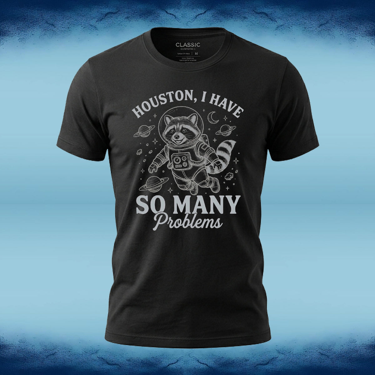 A black short-sleeve graphic t-shirt featuring a white astronaut raccoon design with the text 'HOUSTON, I HAVE SO MANY Problems' on the front, displayed against a blue textured background.