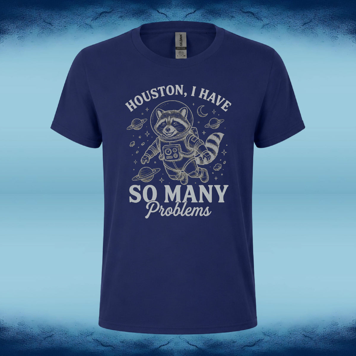 A navy blue short-sleeve t-shirt with a white graphic of a raccoon in an astronaut suit floating in space, surrounded by planets and stars. The text reads 'HOUSTON, I HAVE SO MANY Problems'.