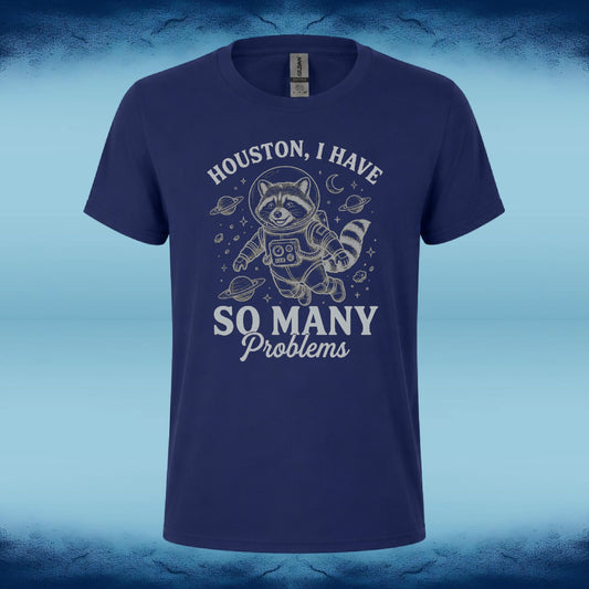 A navy blue short-sleeve t-shirt with a white graphic of a raccoon in an astronaut suit floating in space, surrounded by planets and stars. The text reads 'HOUSTON, I HAVE SO MANY Problems'.