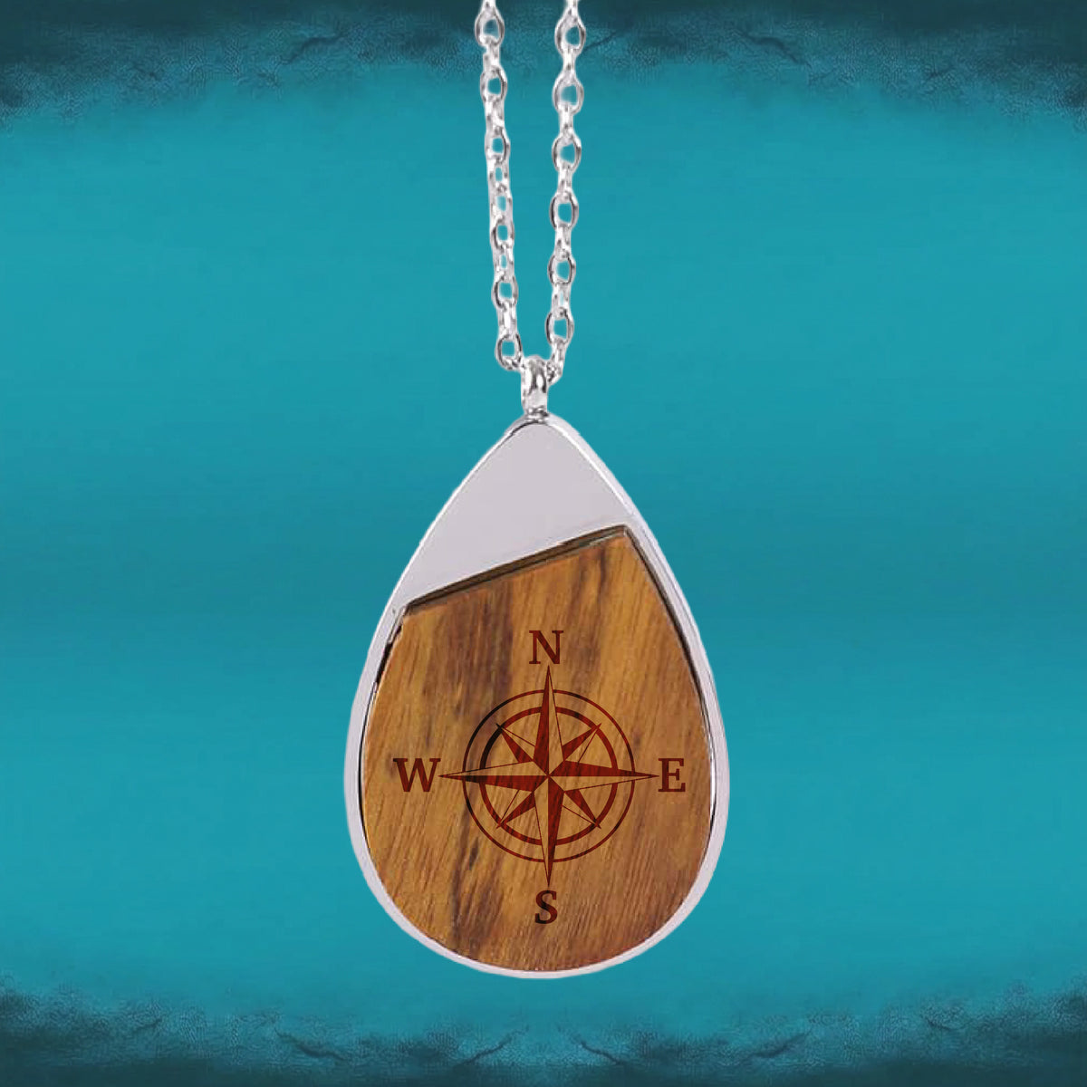 Hero: Compass Engraved Teardrop Pendant necklace with an engraved compass rose set in a teardrop-shaped wood inlay and silver-tone frame.