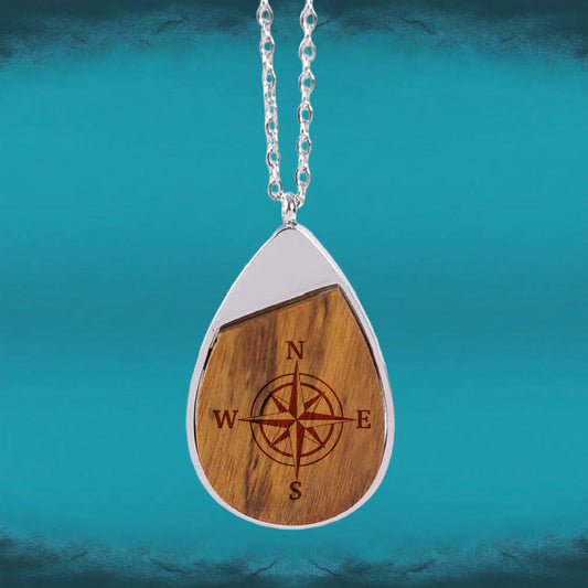Hero: Compass Engraved Teardrop Pendant necklace with an engraved compass rose set in a teardrop-shaped wood inlay and silver-tone frame.