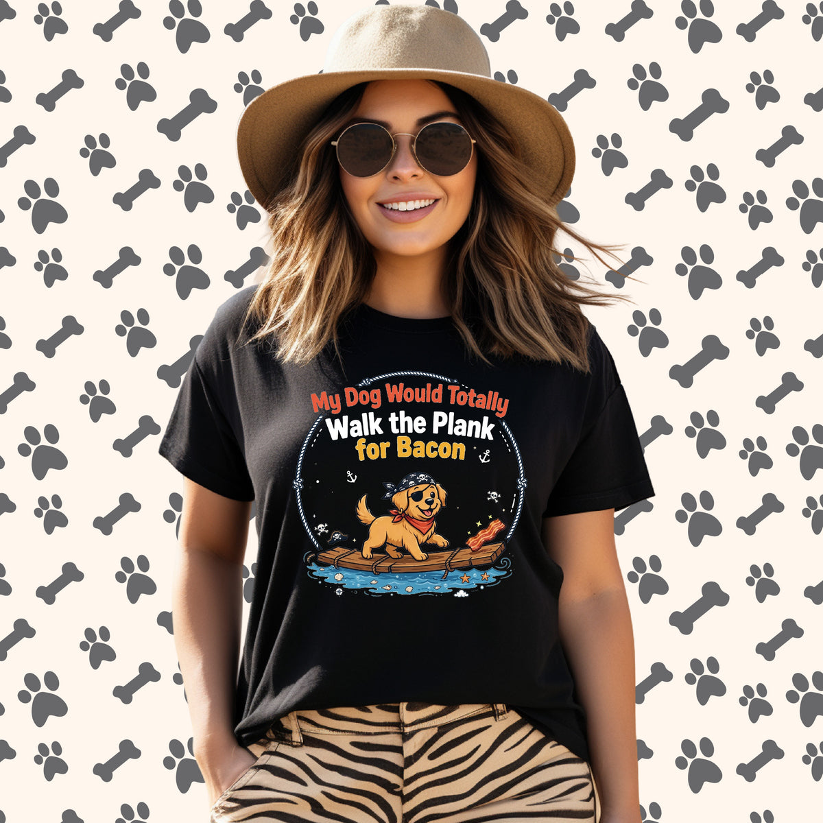A woman wearing a black graphic t-shirt with a cartoon dog on a plank walking over a puddle, with the text 'My Dog Would Totally Walk the Plank for Bacon'. She is wearing a tan hat and sunglasses, paired with tiger-print pants, set against a background pattern of gray paw prints and bones.